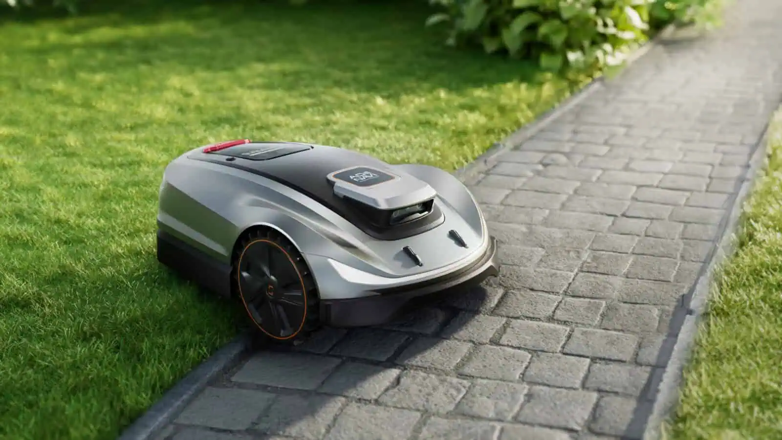 Automated lawn mower on grass near pathway.