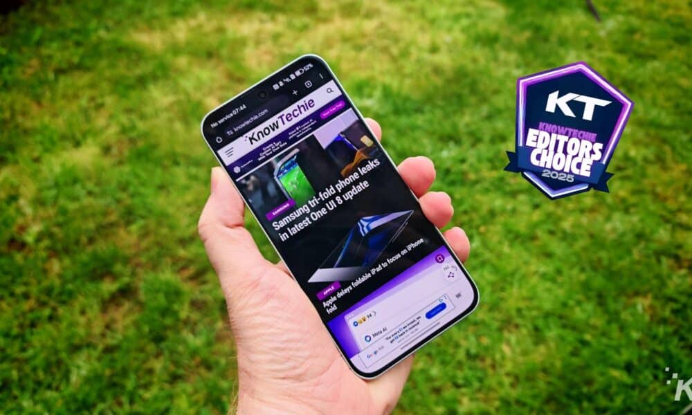 Hand holding smartphone with KnowTechie article displayed.