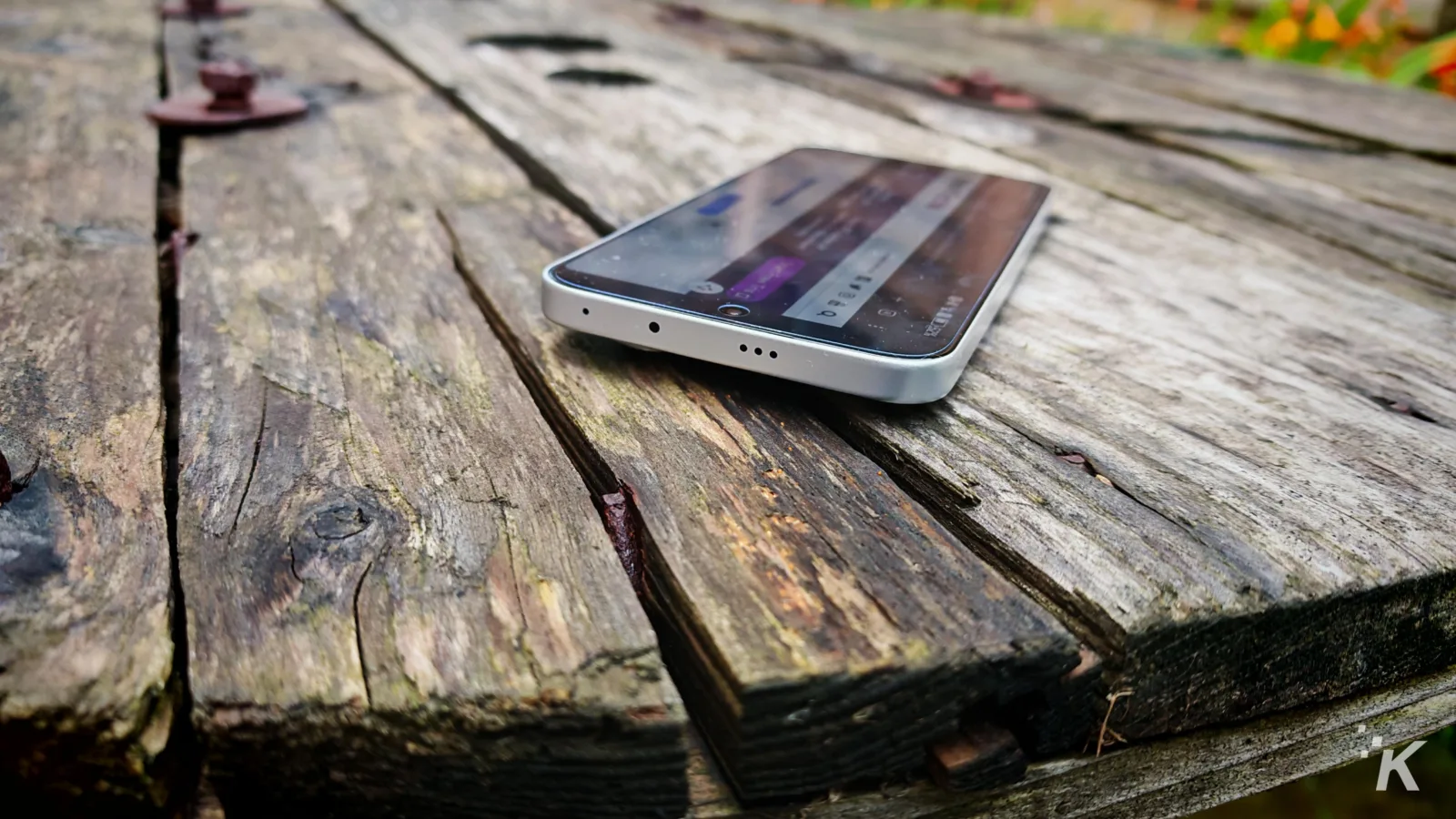 Smartphone on rustic wooden table outdoors.