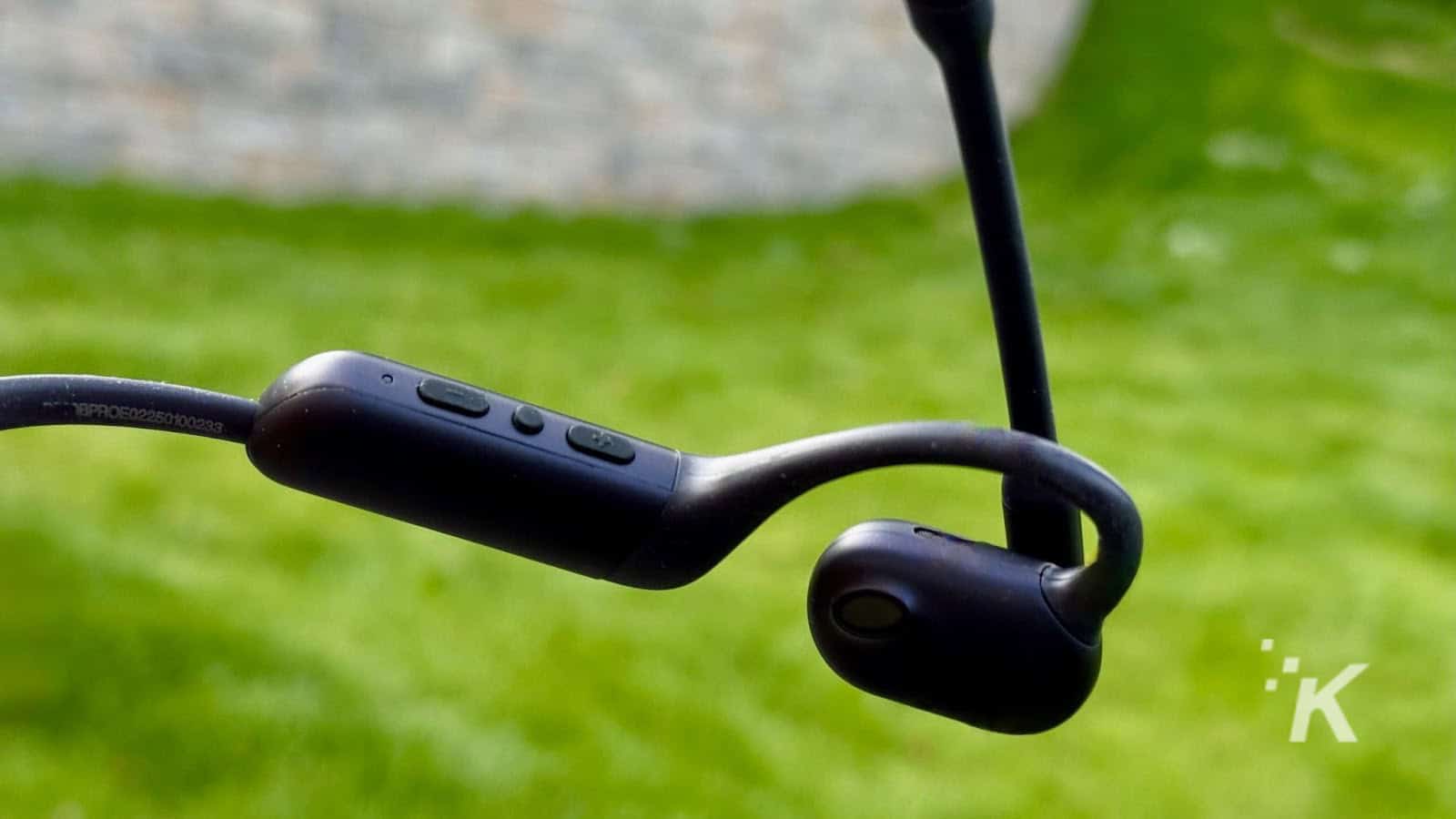 Black wireless earphones against green background.