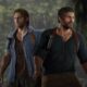 Two men standing with intense expressions in forest.