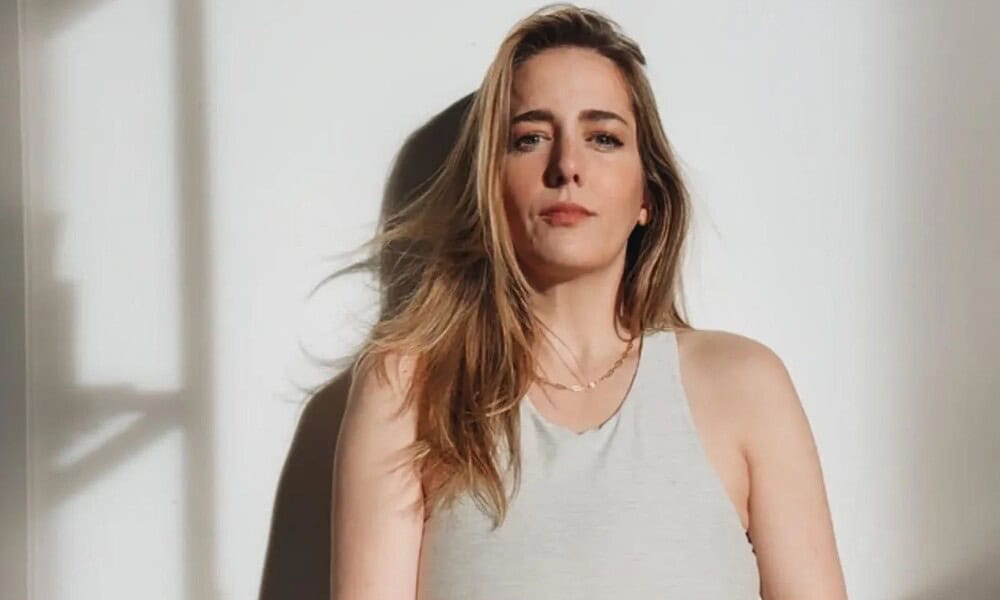 Woman standing against a white wall, natural light.