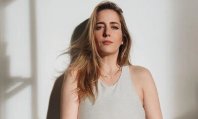 Woman standing against a white wall, natural light.