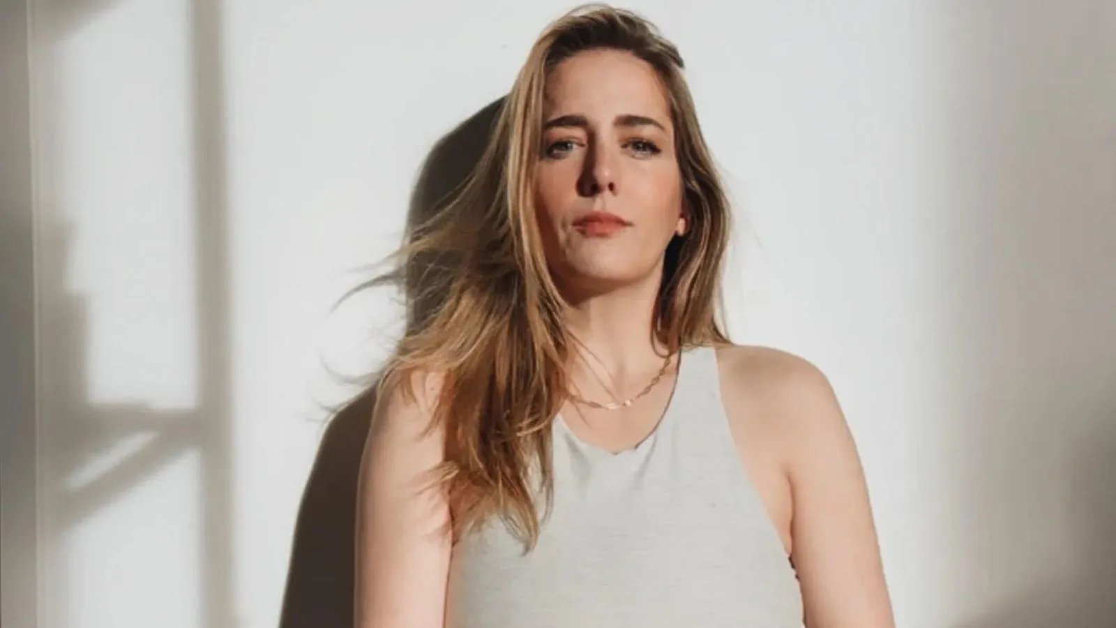 Woman standing against a white wall, natural light.