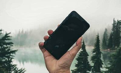 Hand holding smartphone by misty forest lake.