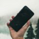 Hand holding smartphone by misty forest lake.