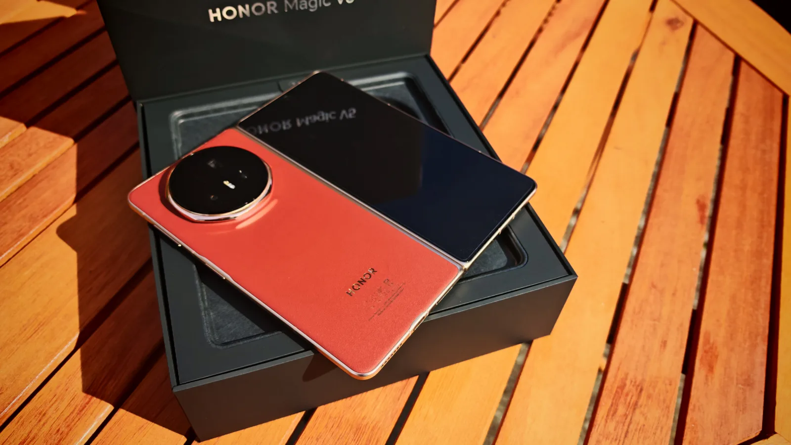 Sleek Honor Magic V smartphone with a dual-tone back and large circular camera module, resting on a black box on a wooden surface, showcasing modern mobile tech design.