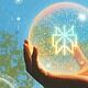 Hand holding glowing sphere against sky background.