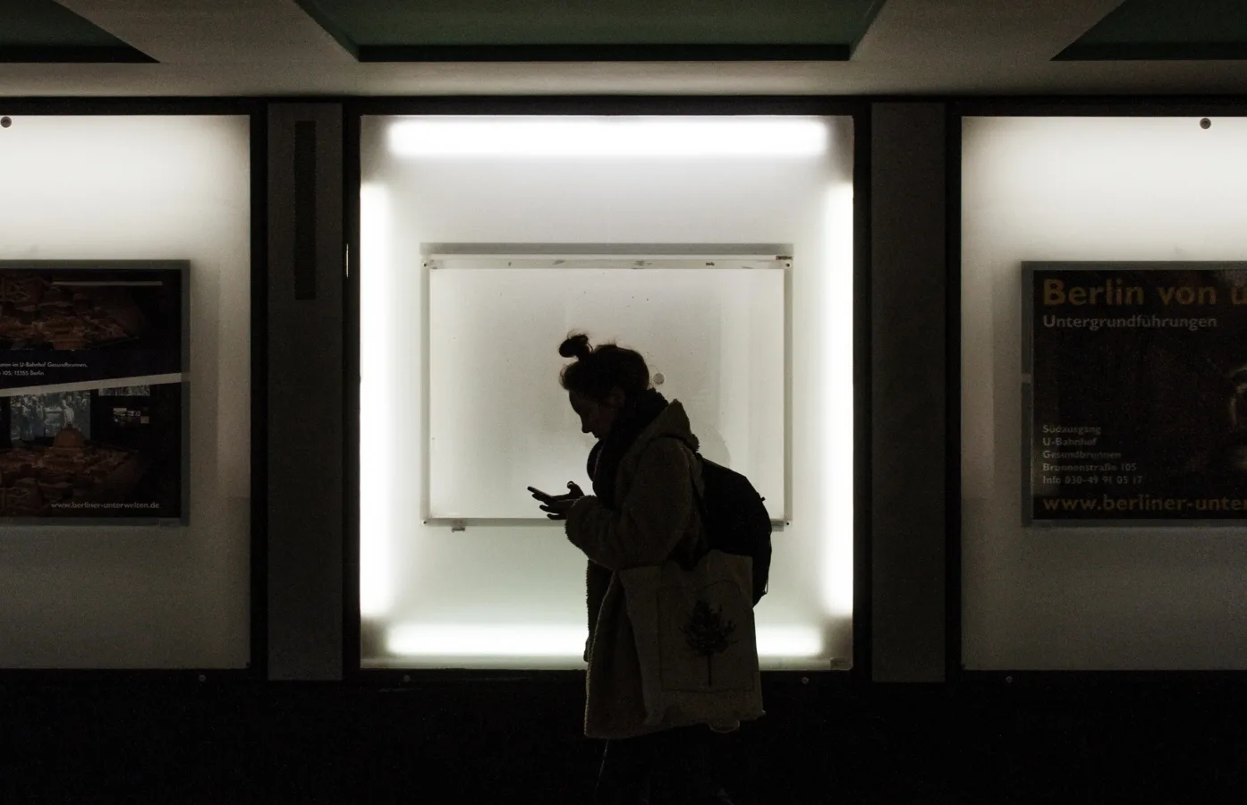 Silhouette of woman using smartphone while waiting at Berlin subway station, backlit display, urban transportation, public transit, commuting scene.