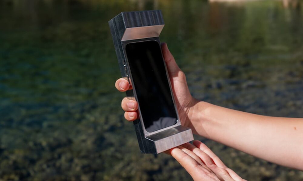 Futuristic smartphone stored in a sleek, metallic case held by a person outdoors near water.