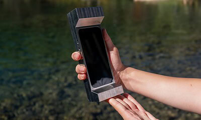 Futuristic smartphone stored in a sleek, metallic case held by a person outdoors near water.