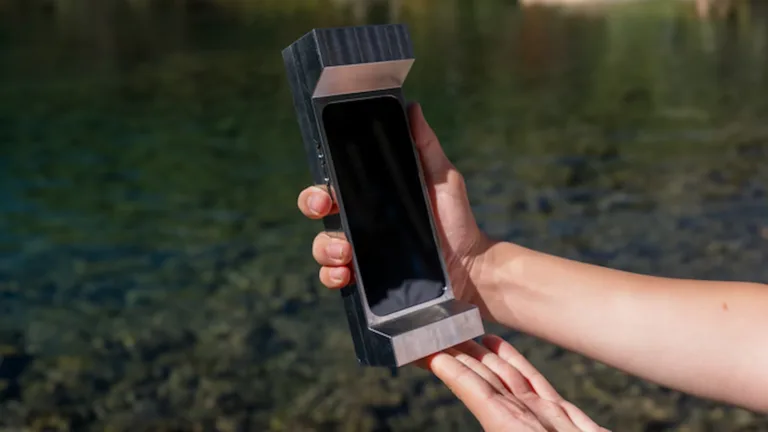 Futuristic smartphone stored in a sleek, metallic case held by a person outdoors near water.