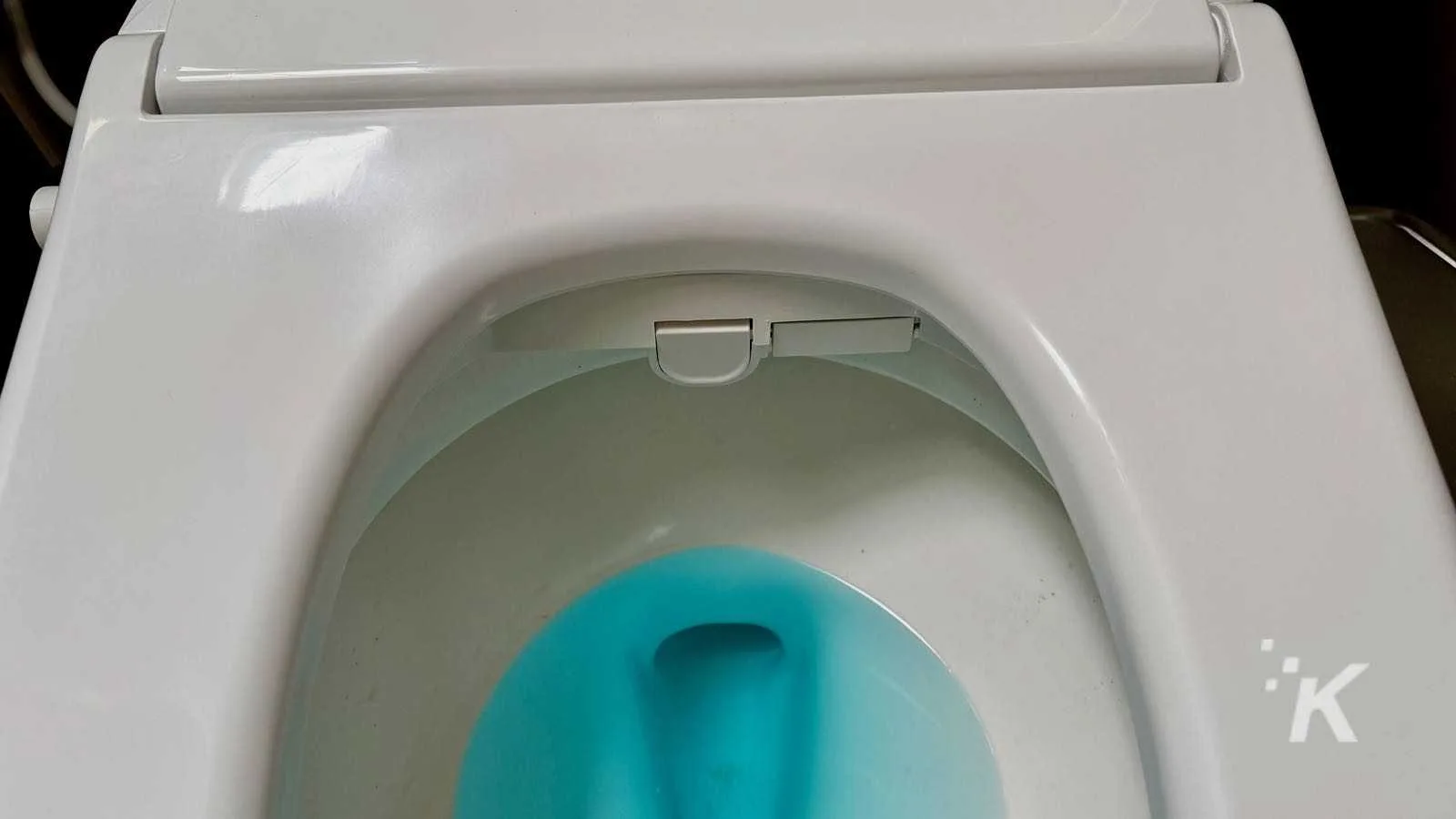 Clean toilet with blue water in bowl