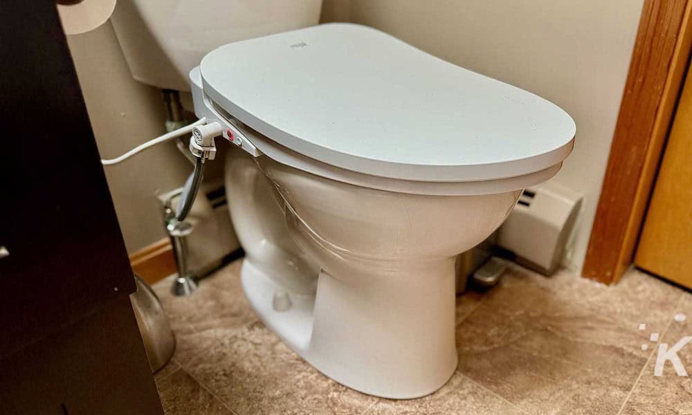 Toilet with a smart lid in a bathroom setting, connecting to power for advanced features like automatic lid opening. Modern bathroom technology integrating smart toilet accessories for enhanced hygiene and convenience.