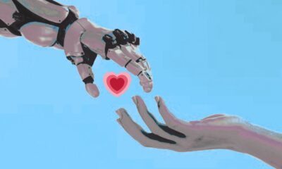 Futuristic robotic hand reaching out to human hand with heart symbol against bright blue sky background.