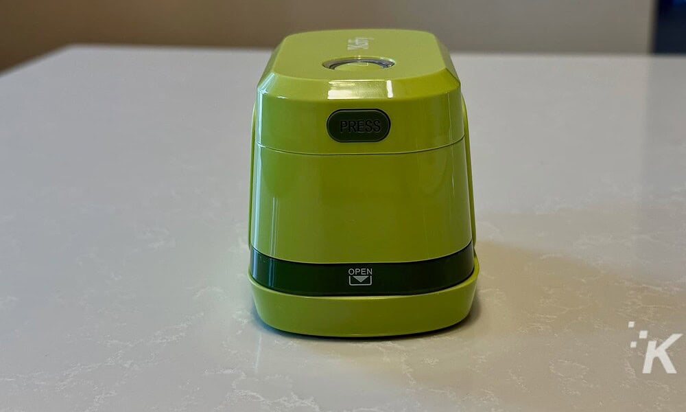 Bright green compact electric pencil sharpener with a black "PRESS" button on top and an "OPEN" compartment at the bottom, placed on a white surface.