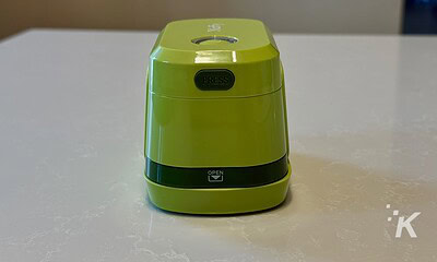 Bright green compact electric pencil sharpener with a black "PRESS" button on top and an "OPEN" compartment at the bottom, placed on a white surface.