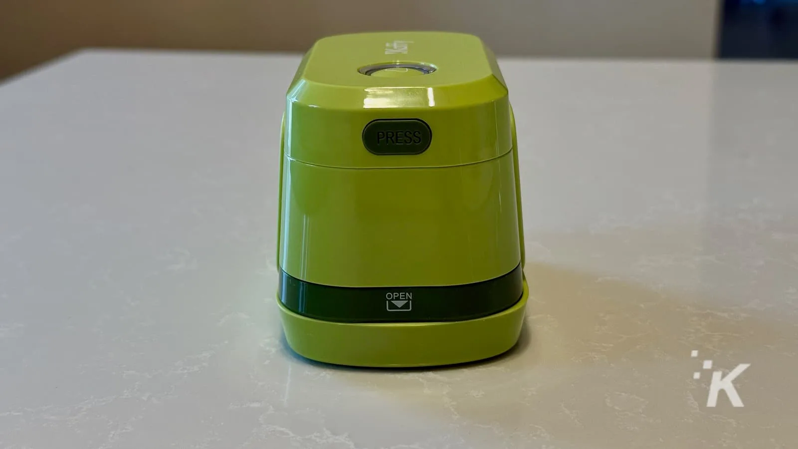 Bright green compact electric pencil sharpener with a black "PRESS" button on top and an "OPEN" compartment at the bottom, placed on a white surface.