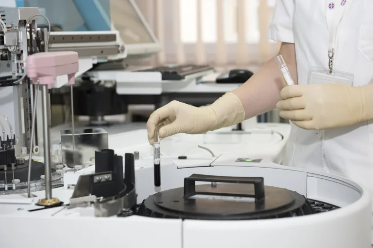 High-tech laboratory scientist handling blood samples using automated medical diagnostic equipment in a medical research facility.