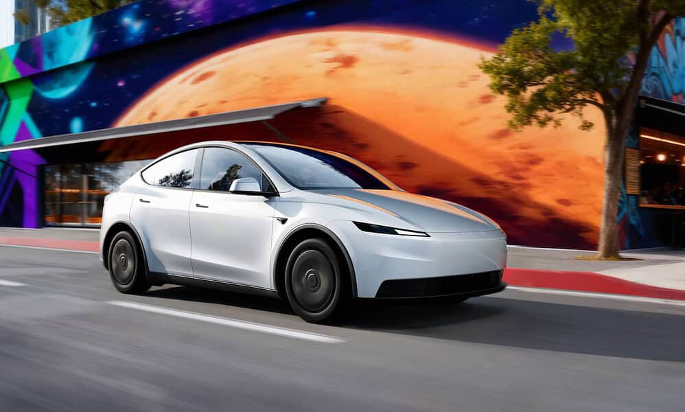 Futuristic white electric car driving past a vibrant mural featuring space and planetary artwork.