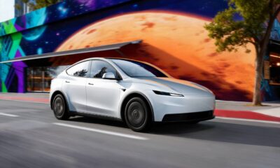 Futuristic white electric car driving past a vibrant mural featuring space and planetary artwork.