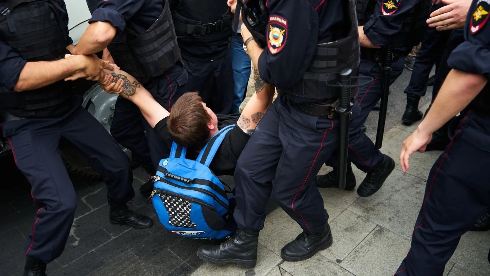 Man being forcibly detained by police officers during protest or altercation.