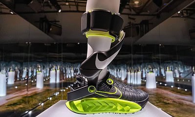 High-tech Nike smart running shoe with attached fitness tracker, displayed in a futuristic exhibit at KnowTechie showcasing innovative wearable technology.