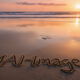 Sunset at the beach with "mail" written in sand on the shore, calm ocean waves, colorful sky, and footprints in the sand, creating a peaceful seaside scene.