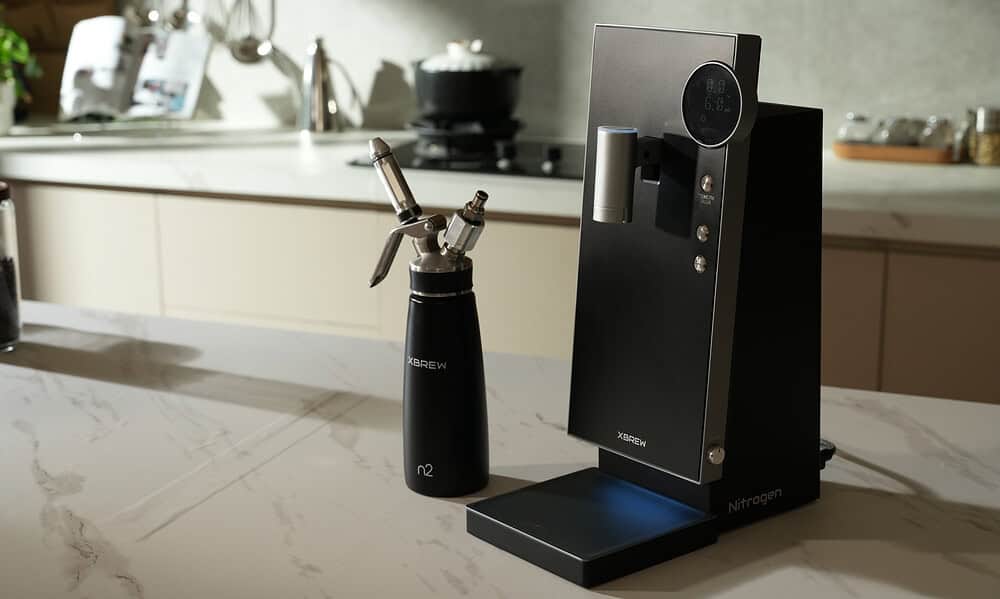 Nitrogen coffee infuser with XBREW branding on a kitchen countertop, modern and sleek device for nitrogen-infused beverages, with a small nitrogen bottle nearby in a bright, contemporary kitchen setting.