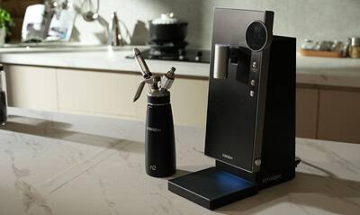 Nitrogen coffee infuser with XBREW branding on a kitchen countertop, modern and sleek device for nitrogen-infused beverages, with a small nitrogen bottle nearby in a bright, contemporary kitchen setting.