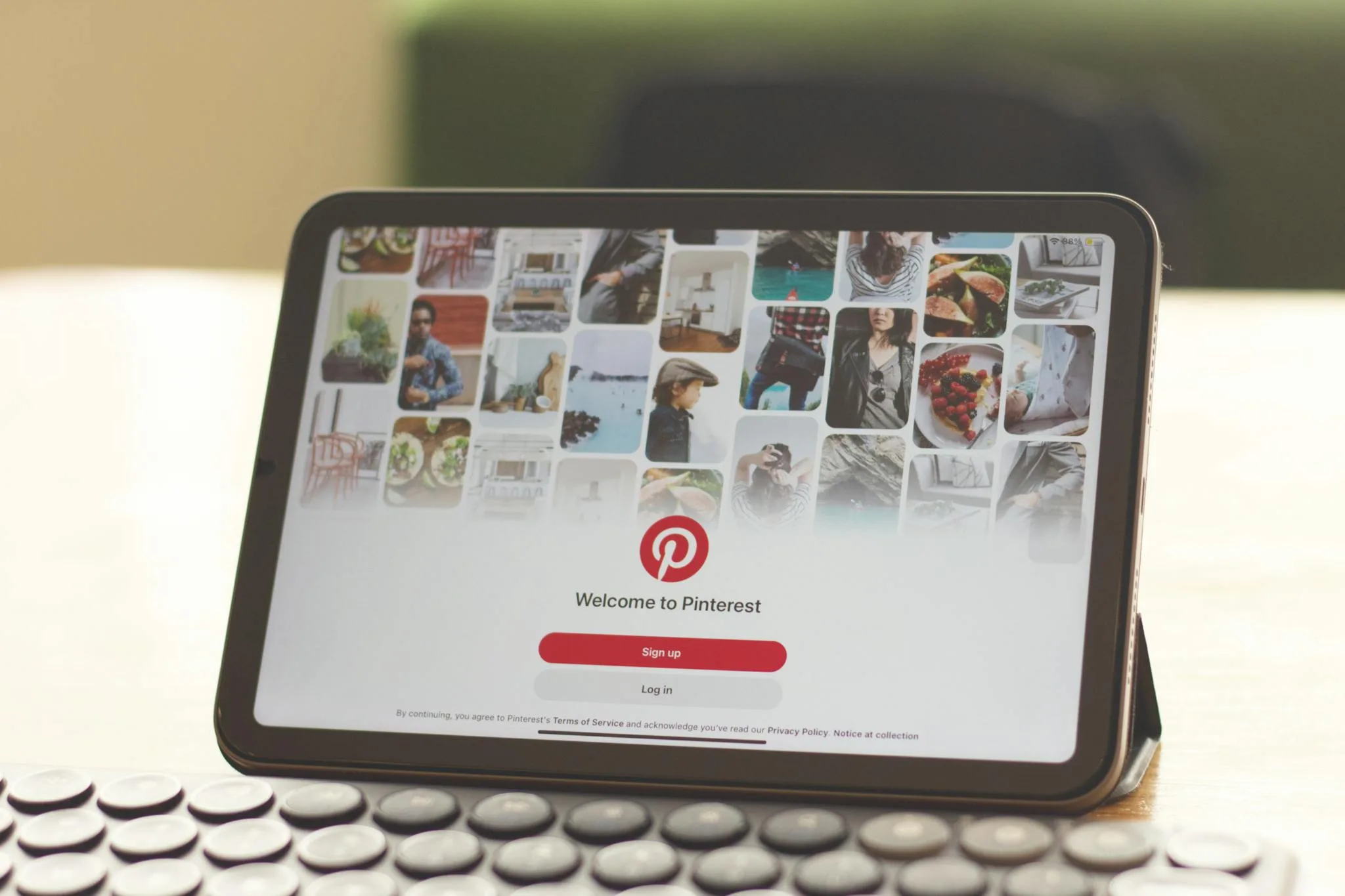An iPad displaying the Pinterest app interface featuring a collage of images including food, fashion, travel, and artwork, with a red "Sign up" button and login option at the center.
