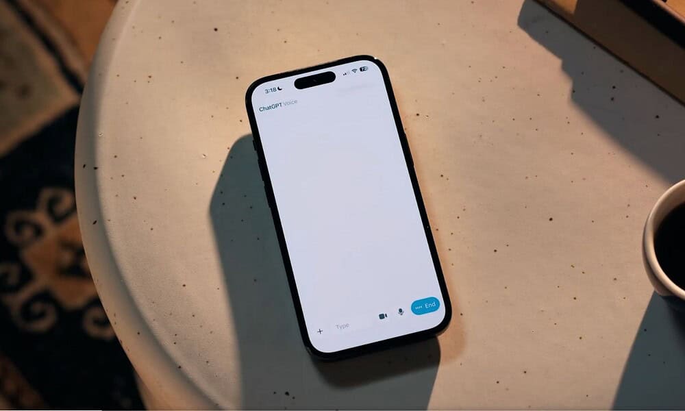 Smartphone with ChatGPT voice app open, ready for conversation, on a beige table with coffee cup nearby, showcasing AI technology and digital assistant features for modern communication.