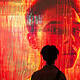 A person observing a large digital art installation featuring a futuristic, glowing human face in red and orange hues, representing technology and innovation themes.