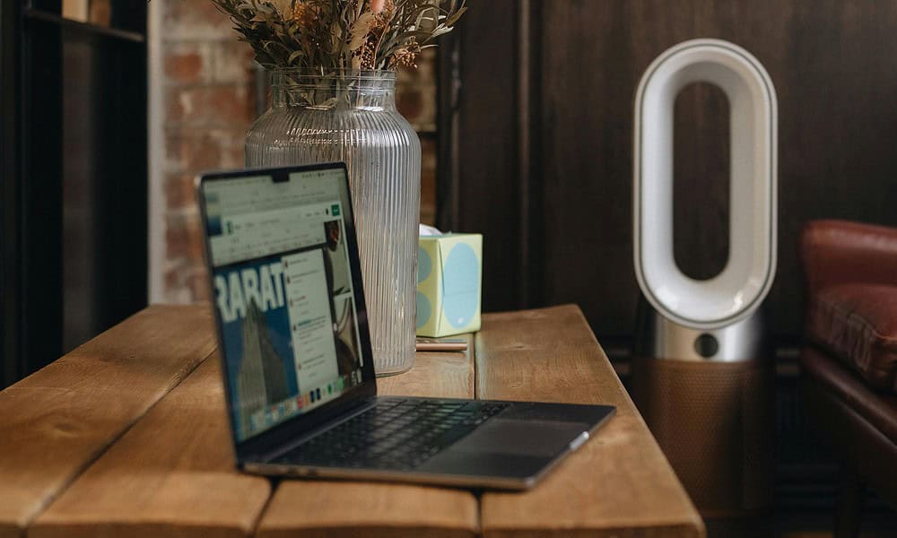 Laptop on table next to air purifier and vase.
