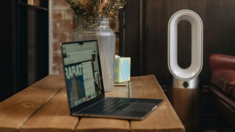 Laptop on table next to air purifier and vase.