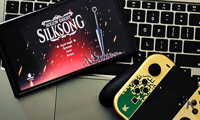 Vivid image of the Silksonic game menu displayed on a smartphone screen, with Nintendo Switch controllers and a keyboard in the background, highlighting gaming accessories and entertainment technology.