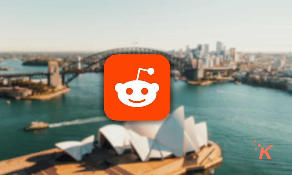 Reddit logo displayed prominently against a blurred background of Sydney’s iconic bridge and Opera House, emphasizing social media, discussion forums, and internet culture.