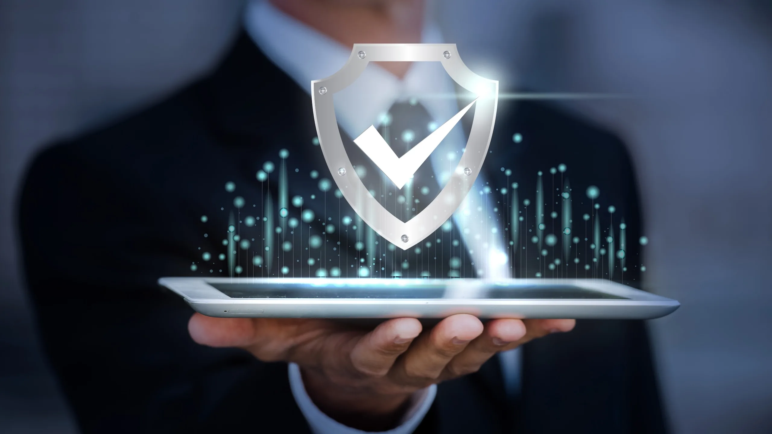 Cybersecurity illustration with shield icon and checkmark displayed above a person's hand holding a tablet, symbolizing digital protection, cyber defenses, and data security in technology.