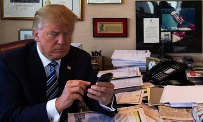 A political figure, possibly Donald Trump, focused on his mobile device amidst a busy work environment.