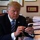 A political figure, possibly Donald Trump, focused on his mobile device amidst a busy work environment.